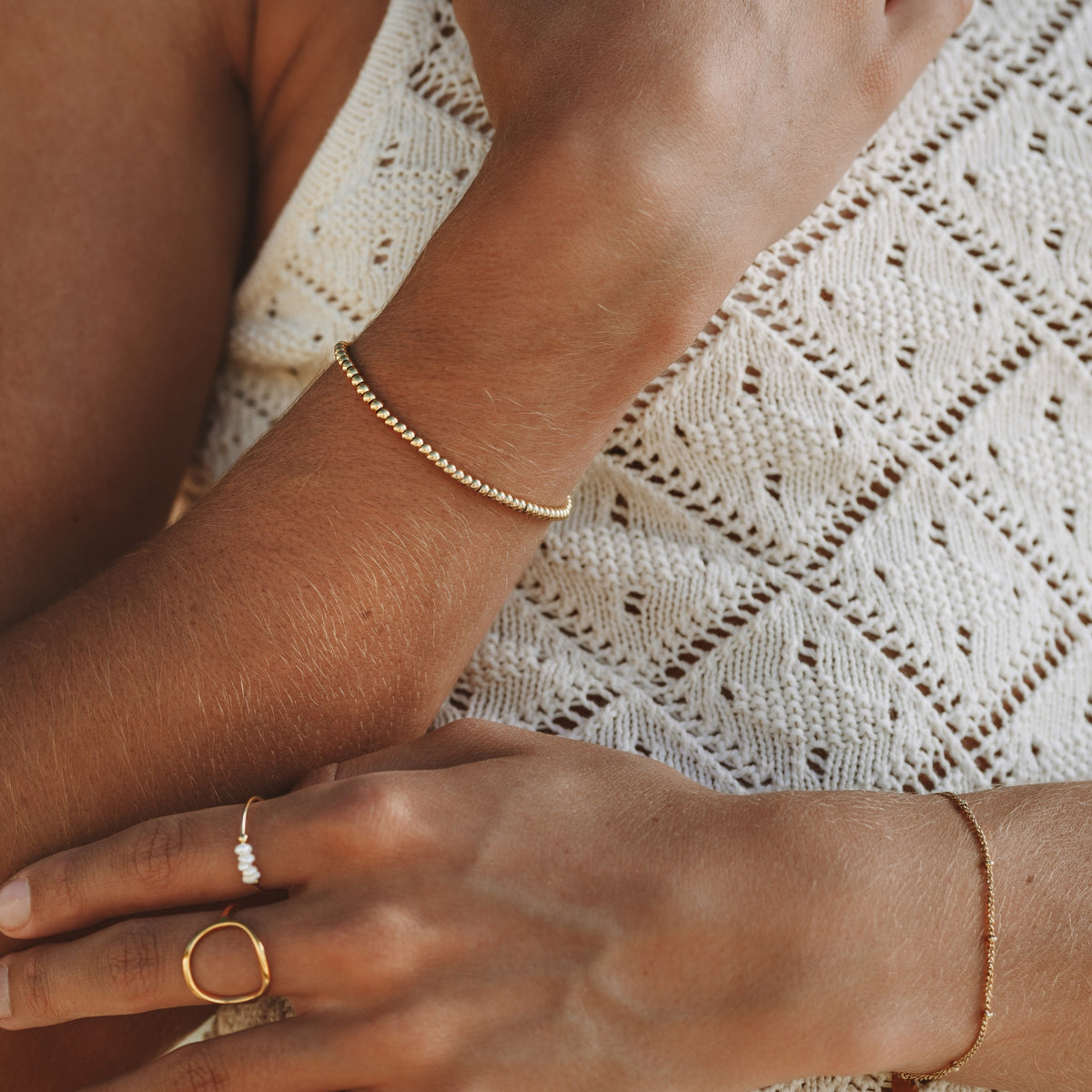 Gold beaded bracelet worn on the wrist with dainty gold rings