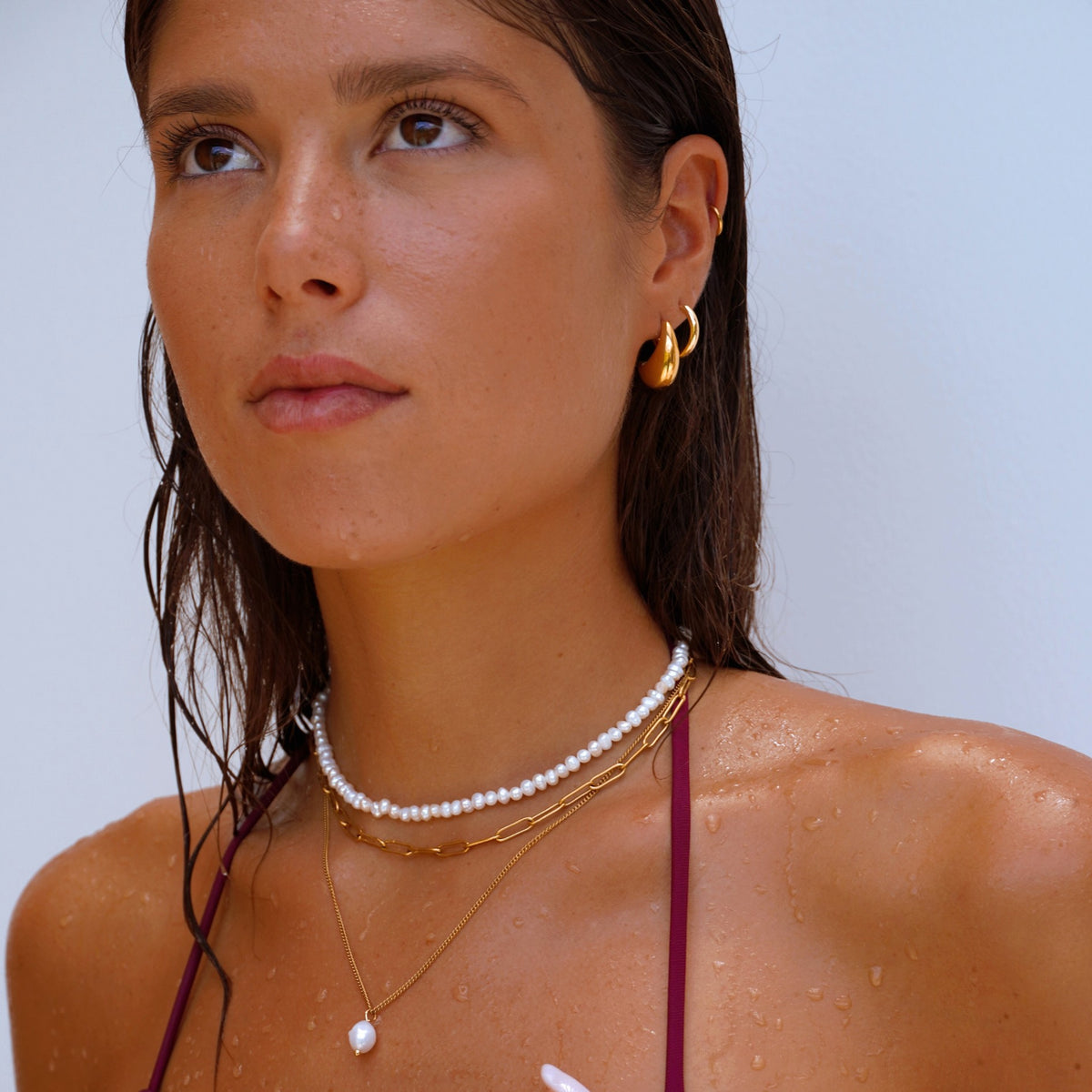 Model with wet hair wearing a freshwater pearl choker layered with gold necklaces and gold hoops